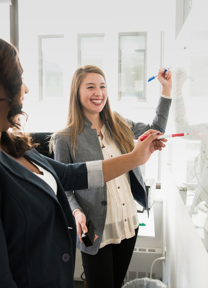 Two business women writing on a board during a workshop with their strategic marketing agency